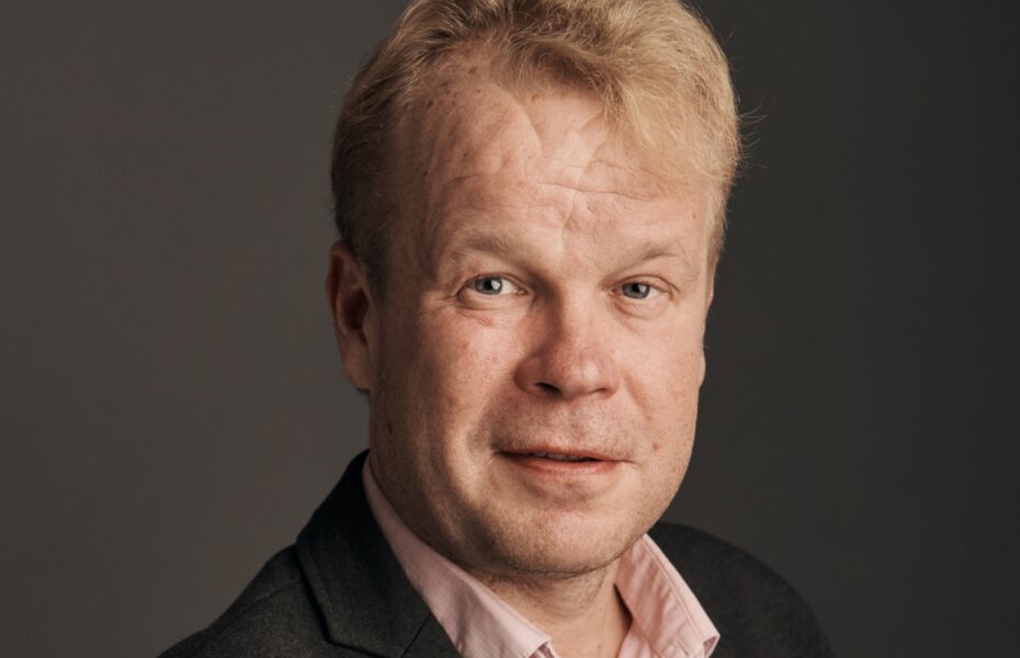 Mies kauluspaidassa ja pikkutakissa. Lähikuva kasvoista.