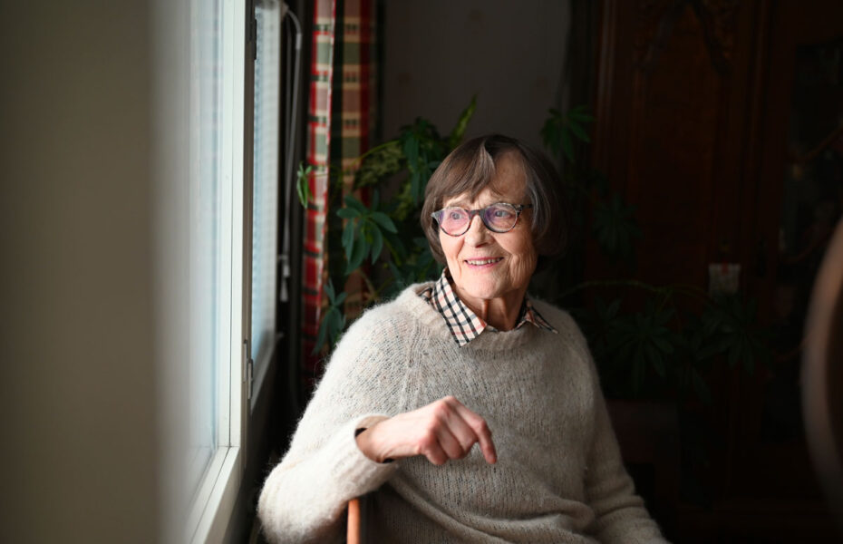 Nainen istuu sohvalla ikkunan ääressä ja katsoo ulos.