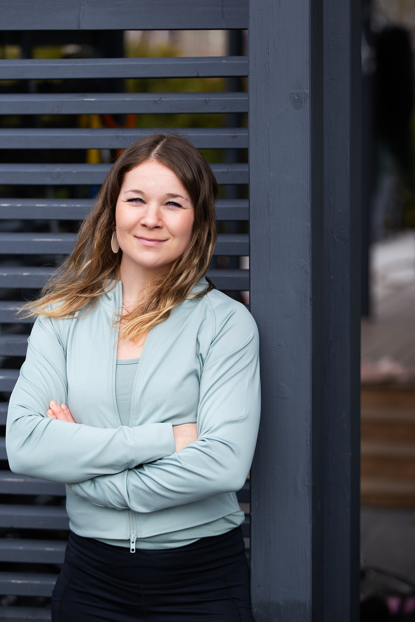 Nainen nojaa sinistä aitaa vasten ja hymyilee. Ulkona.