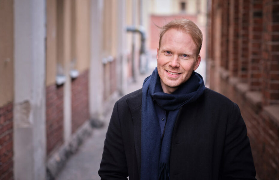 Kalle Mäenpää seisoo kadulla kahden talon välissä.