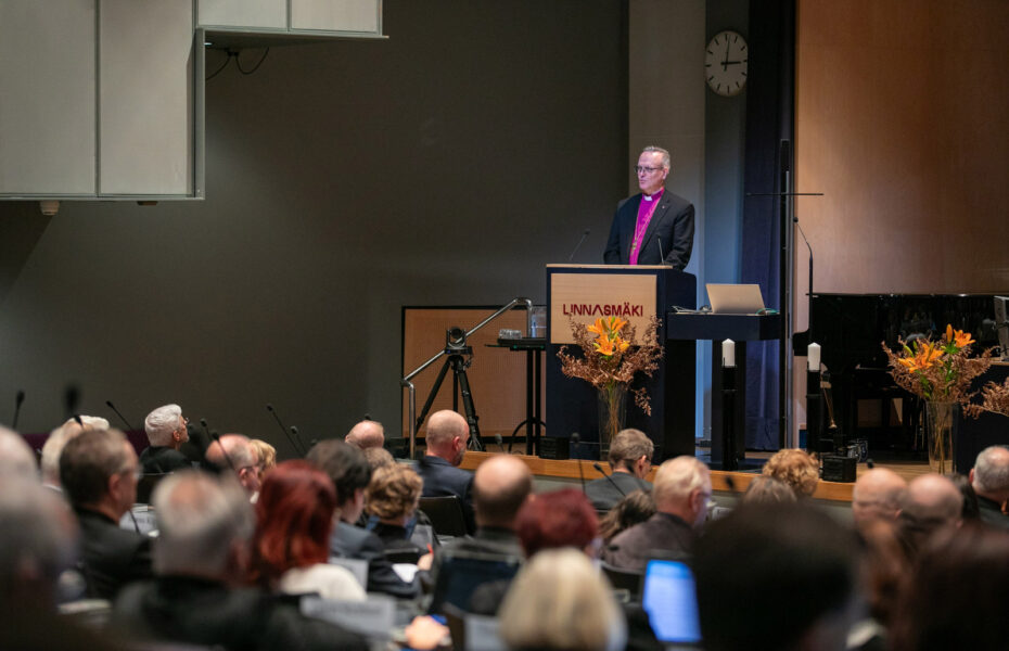 Arkkipiispa puhujapöntön takana. Etualalla kirkolliskokousedustajia