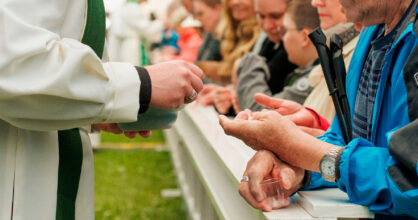 Pappi antaa ehtoollista miehelle, jonka käsi on ojennettu. Ehtoollisenviettäjät ovat suuressa teltassa.