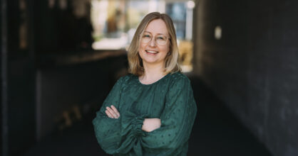 Nainen pitää käsiä puuskassa ja hymyilee.