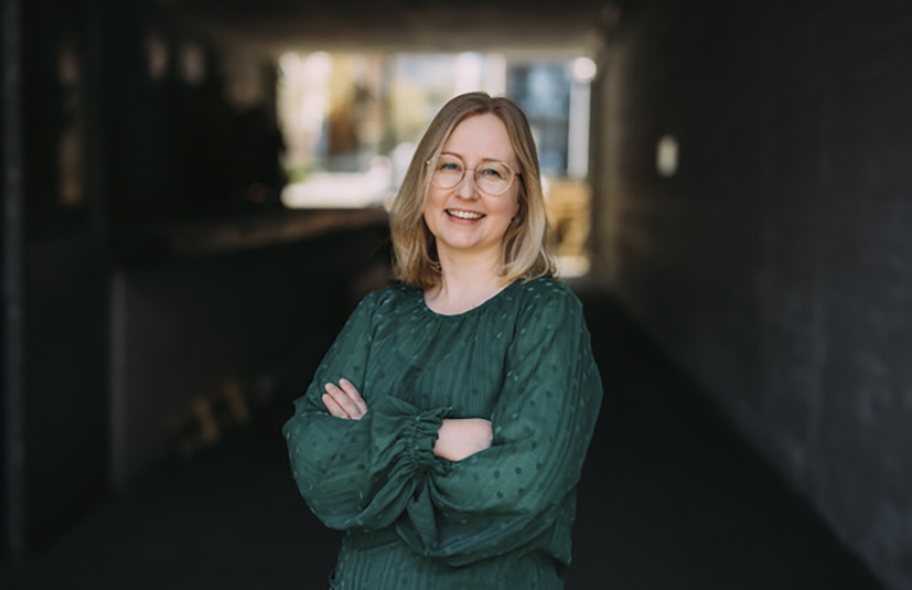 Nainen pitää käsiä puuskassa ja hymyilee.