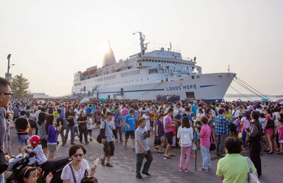 Lähetyslaiva satamassa. Laivan edustalla on tuhansittain ihmisiä.