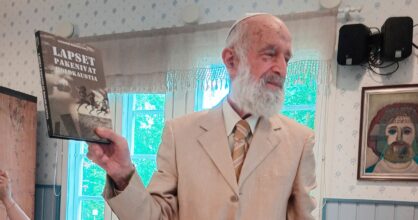 Valkopartainen mies pitää kädessään kirjaa, jossa lukee: "Lapset pakenivat holokaustia".