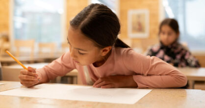 Tyttö piirtää pulpetilla paperiin.