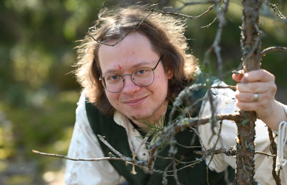 Miehellä on silmälasit ja olkapäille ulottuvat kiharat hiukset. Hän hymyilee.