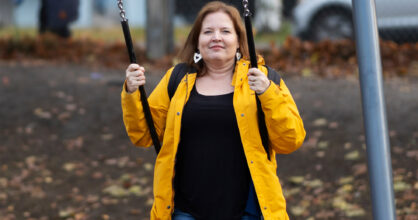 Nainen istuu keinussa ulkona ja hymyilee.