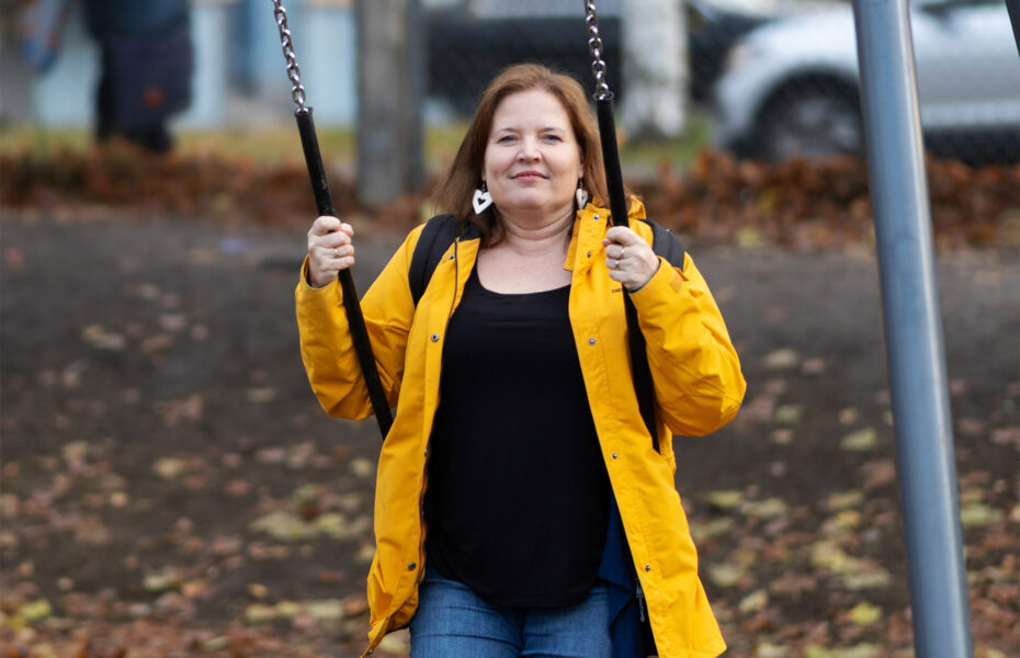 Nainen istuu keinussa ulkona ja hymyilee.