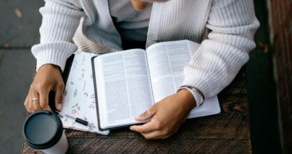 Kuvassa joku lukee Raamattua pöydällä ja vieressä on kahvikuppi.