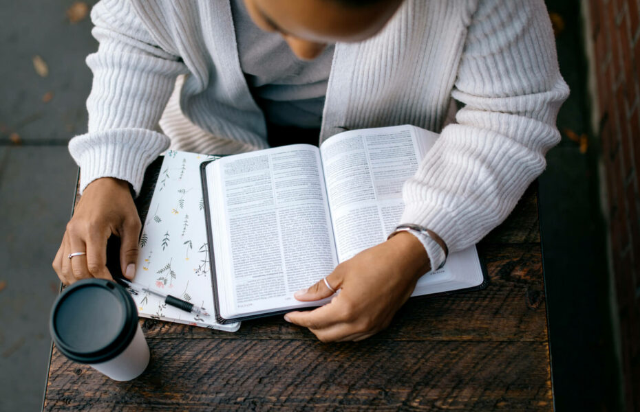 Kuvassa joku lukee Raamattua pöydällä ja vieressä on kahvikuppi.