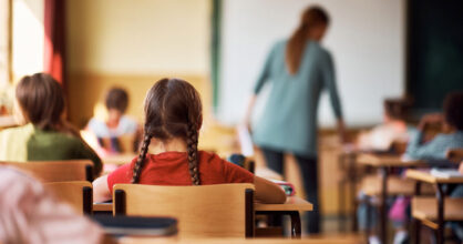 Luokkahuone, jossa on opettaja ja oppilaita takaapäin kuvattuna.