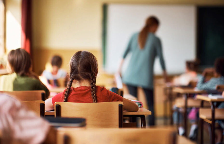 Luokkahuone, jossa on opettaja ja oppilaita takaapäin kuvattuna.