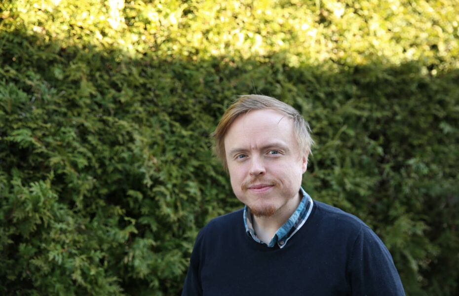 Ylävartalokuvassa Martti Pyykönen seisoo vihreän pensaan edessä ja katsoo kameraan.