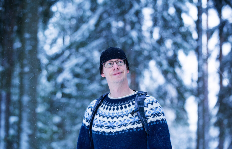 Villapaitaan ja pipoon pukeutunut Matti Korhonen talvisessa metsässä.