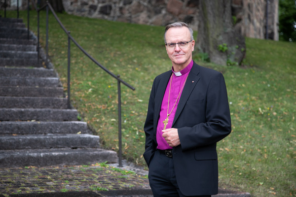 Kuvassa arkkipiispa Tapio Luoma seisoo kirkon edessä virkapuvussaan ja katsoo kameraan.
