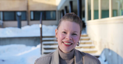 Miia Eklund hymyilee. Taustalla on kerrostalo, jonka pihalla on lunta.