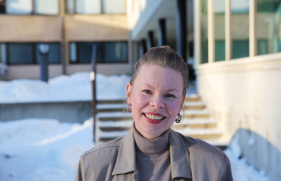 Miia Eklund hymyilee. Taustalla on kerrostalo, jonka pihalla on lunta.
