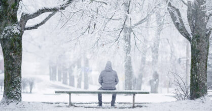 Mies istuu penkillä lumisessa puistossa.