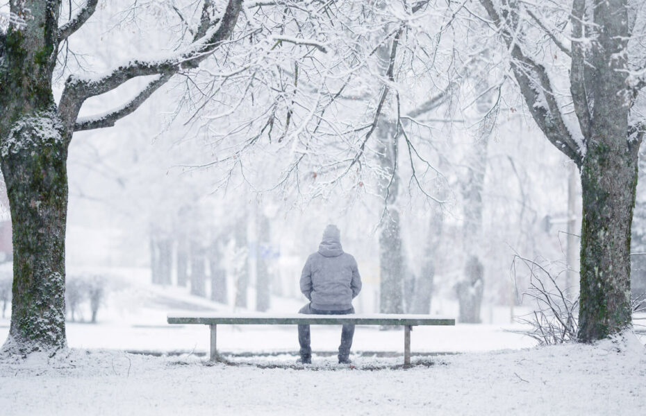 Mies istuu penkillä lumisessa puistossa.
