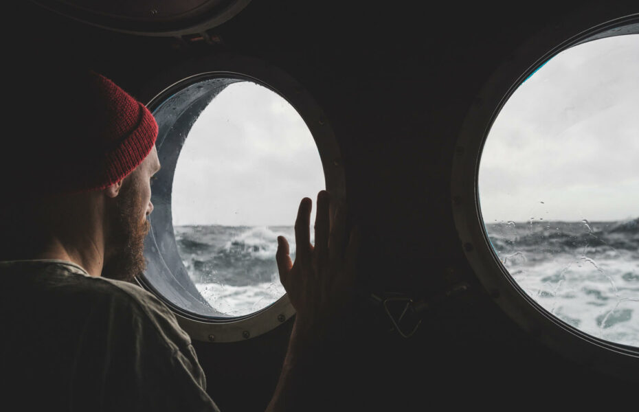 Mies katsoo laivan pyöreästä ikkunasta aaltoja.