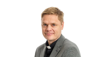 Mika Lehtinen papin puvussa katsoo kameraan.