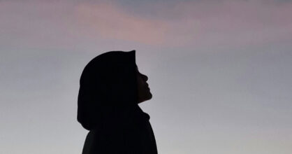 Musliminaisen siluetti. Nainen katsoo kohti taivasta.