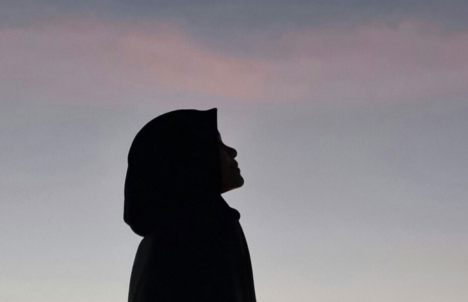 Musliminaisen siluetti. Nainen katsoo kohti taivasta.