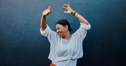 Nainen hymyilee ja hän on nostanut kätensä ilmaan.