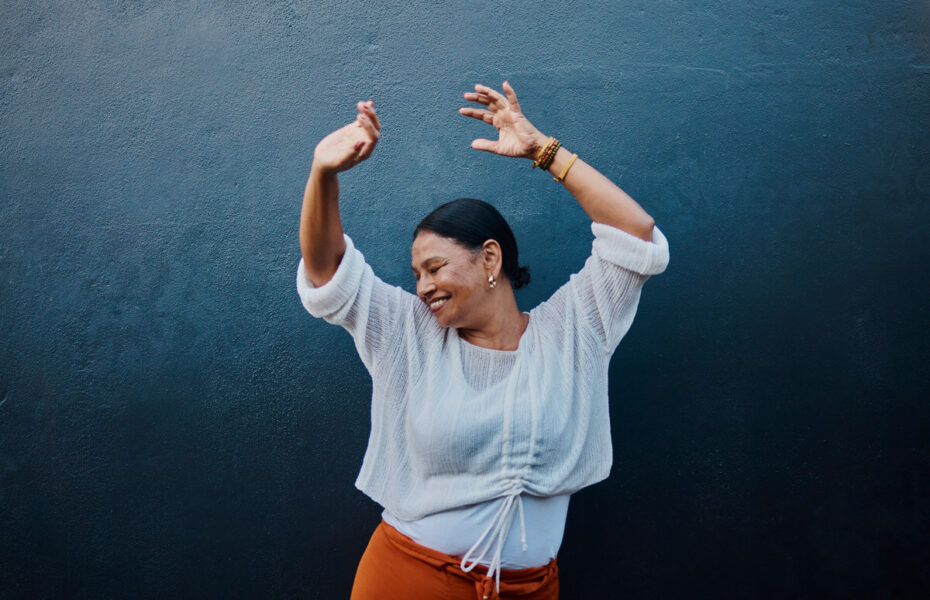 Nainen hymyilee ja hän on nostanut kätensä ilmaan.