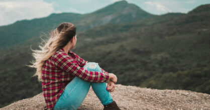 Nainen istuu kivellä ja katsele vuoristoa.