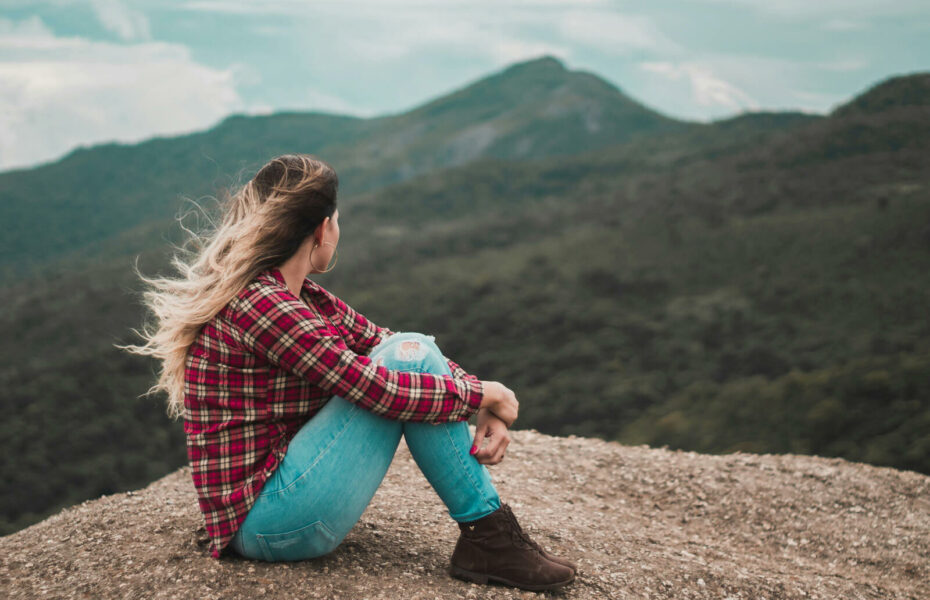Nainen istuu kivellä ja katsele vuoristoa.