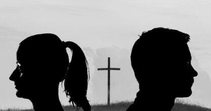 Mustavalkoinen kuva. Nainen ja mies katsovat eri suuntiin. Heidän välissään on risti.