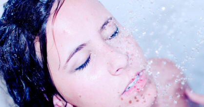 Naisen kasvoille putoaa suihkun vesipisaroita.