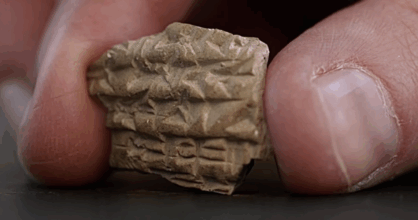 Peukalon ja etusormen välissä on kivenpala, jossa on kirjoitusta.