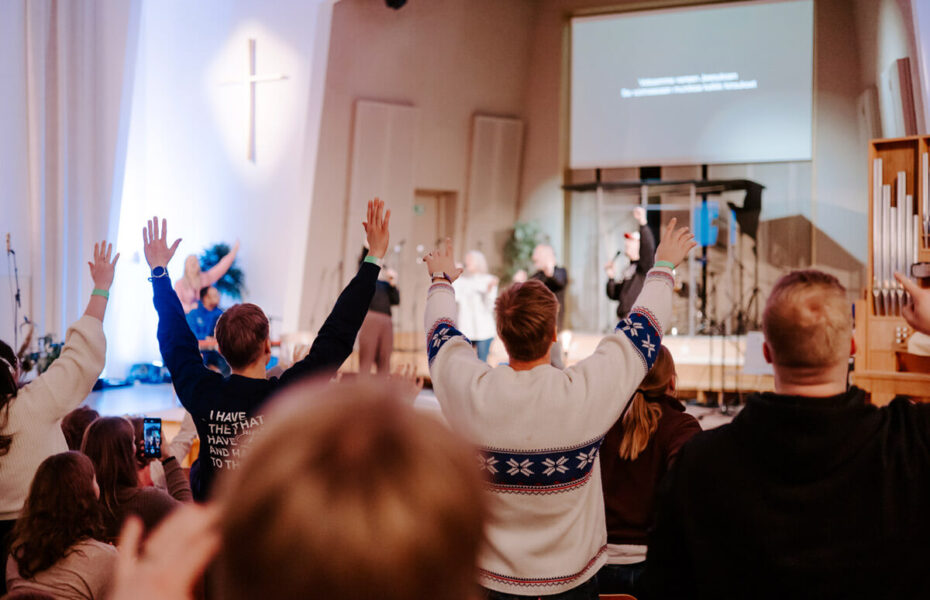 Nuoret ylistävät kädet kohotettuina kohti kattoa.