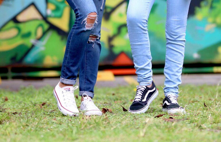 Kaksi nuorte seisoo nurmikolla. Vain heidän jalkansa reidestä alaspäin näkyvät. Heillä on farkut ja tennarit.