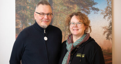 Mies ja nainen hymyilevät sisällä. Naisella lukee hupparissa "nuorisotiimi".