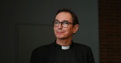 Mies, jolla on silmälasit ja musta papinpaita.