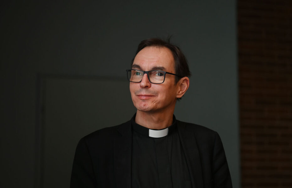 Mies, jolla on silmälasit ja musta papinpaita.