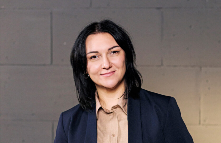 Olena hymyilee. Hänellä on tummat hiukset, jotka yltävät hartioille saakka.