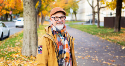 Valkopartainen silmälasipäinen mies syyskelissä keltaisessa takissaan.