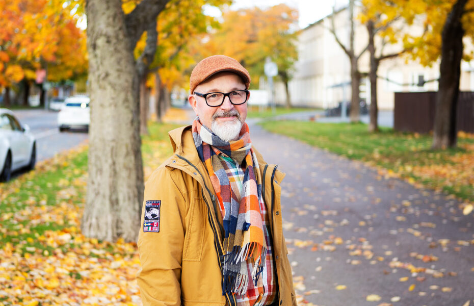 Valkopartainen silmälasipäinen mies syyskelissä keltaisessa takissaan.