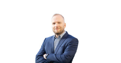 Santeri Marjokorpi hymyilee. Hänellä on paita ja puvun takki.