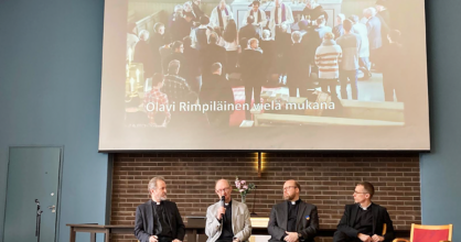 Neljä miestä keskustelee lavalla. Paneelikeskustelu.
