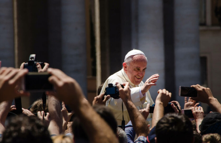 Paavi Franciscus heiluttaa kättään ihmisten keskellä.