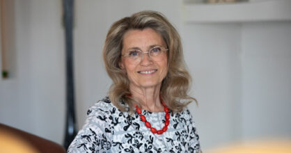 Päivi Räsänen hymyilee. Hänellä on silmälasit ja punainen kaulakoru.