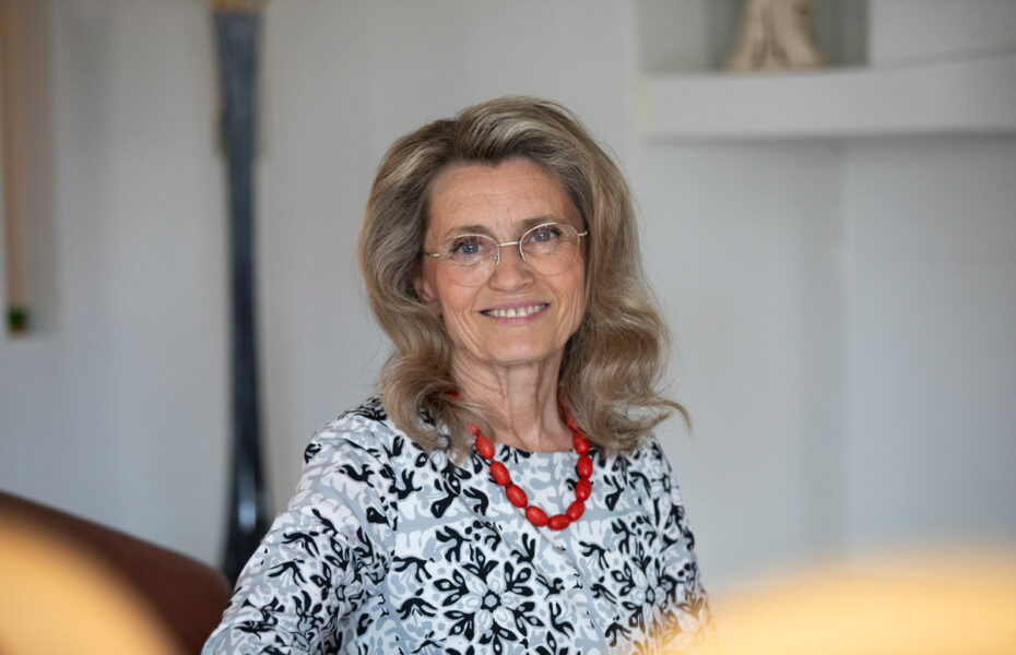 Päivi Räsänen hymyilee. Hänellä on silmälasit ja punainen kaulakoru.