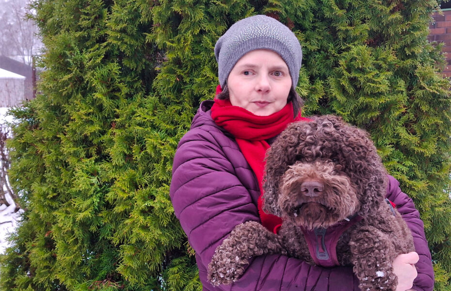 Nainen pitää ruskeaa koiraa sylissään.